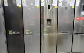 Rząd nowych lodówek w kolorach srebrnym i czarnym, z widocznymi etykietami energetycznymi i naklejkami promocyjnymi, prezentowany w sklepie.