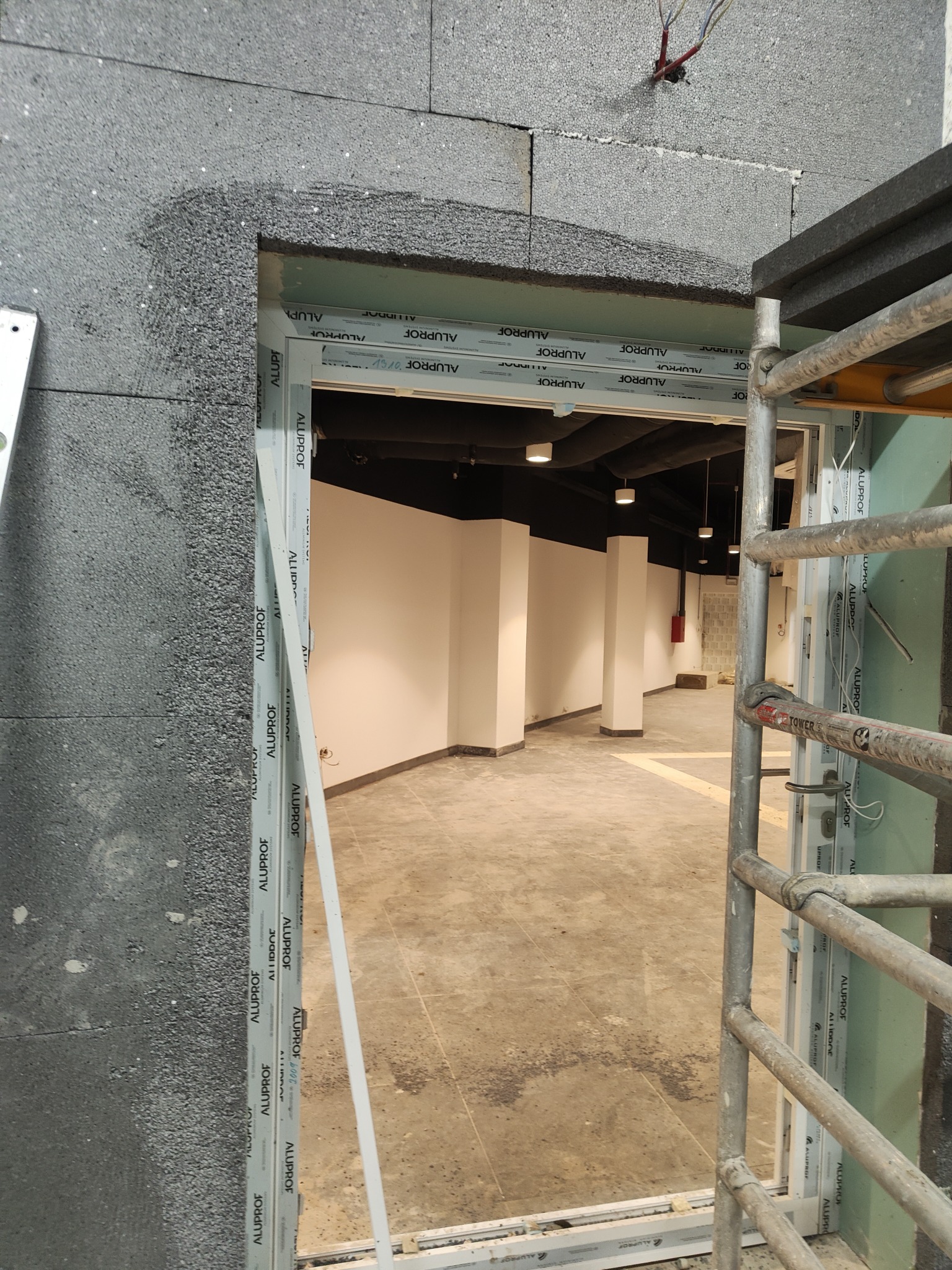 Otwór okienny w trakcie ocieplania ścian zewnętrznych styropianem grafitowym, widoczne rusztowanie i wnętrze budynku w stanie surowym.