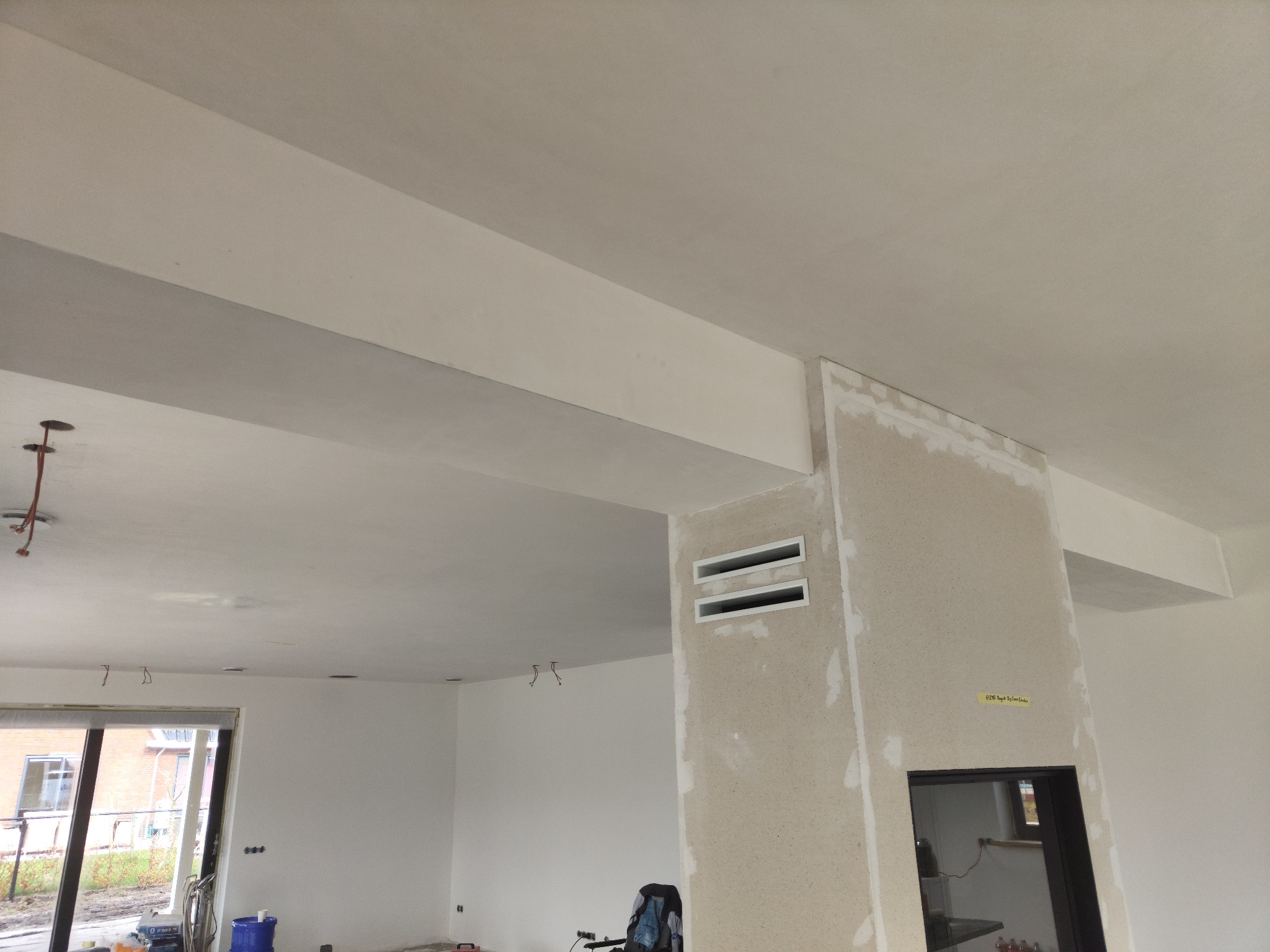 Wnętrze w trakcie remontu: sufit z widocznymi belkami konstrukcyjnymi, ściana z surową fakturą i wnękami wentylacyjnymi, widoczne ślady szpachlowania, przygotowanie do malowania.