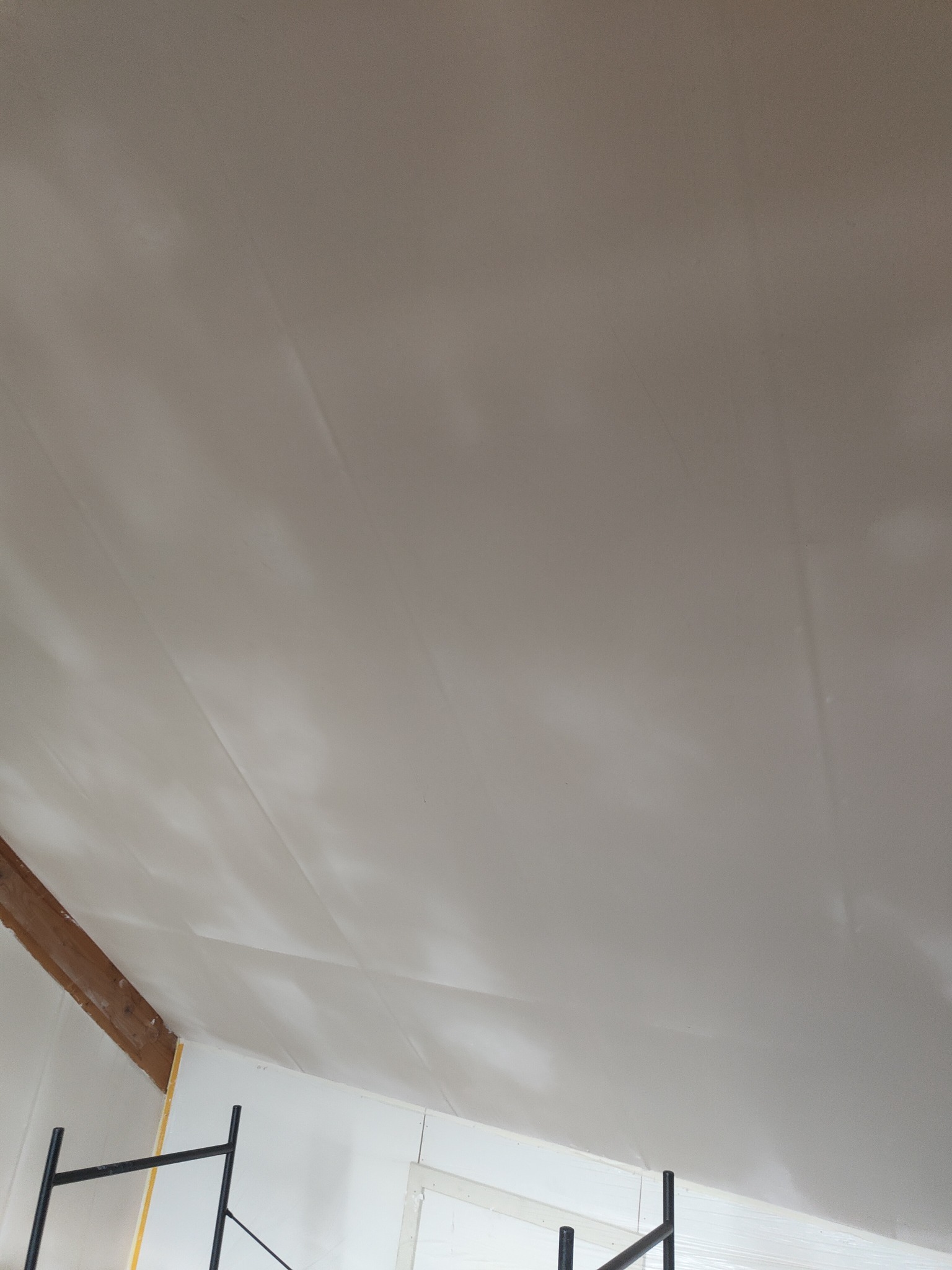 Biały sufit poddasza wykończony płytami gipsowo-kartonowymi, widoczny fragment drewnianej belki stropowej i rusztowanie malarskie.