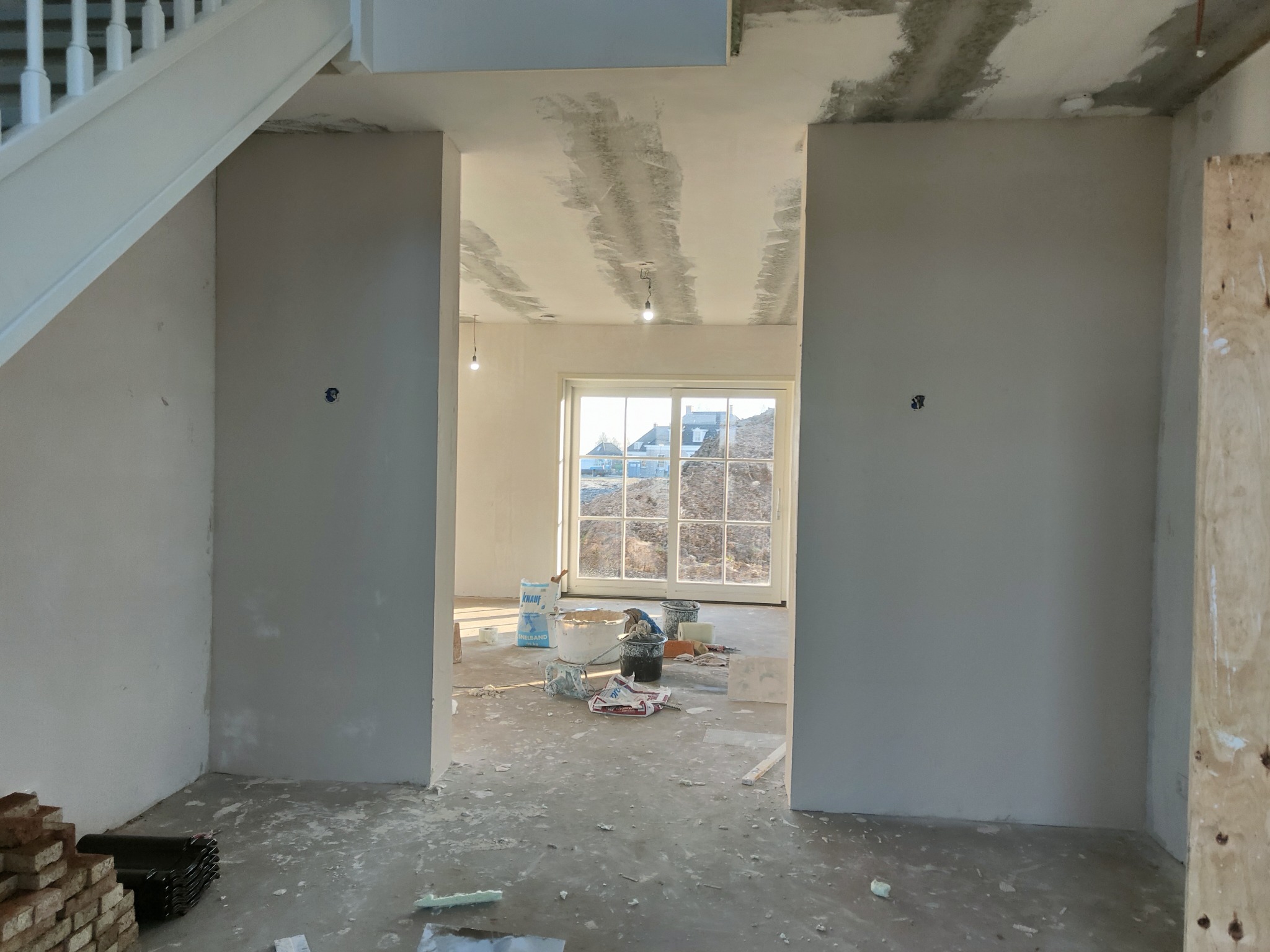 Wnętrze domu w trakcie prac wykończeniowych: szpachlowane ściany i sufit, widoczne materiały budowlane, przygotowane do dalszych prac.