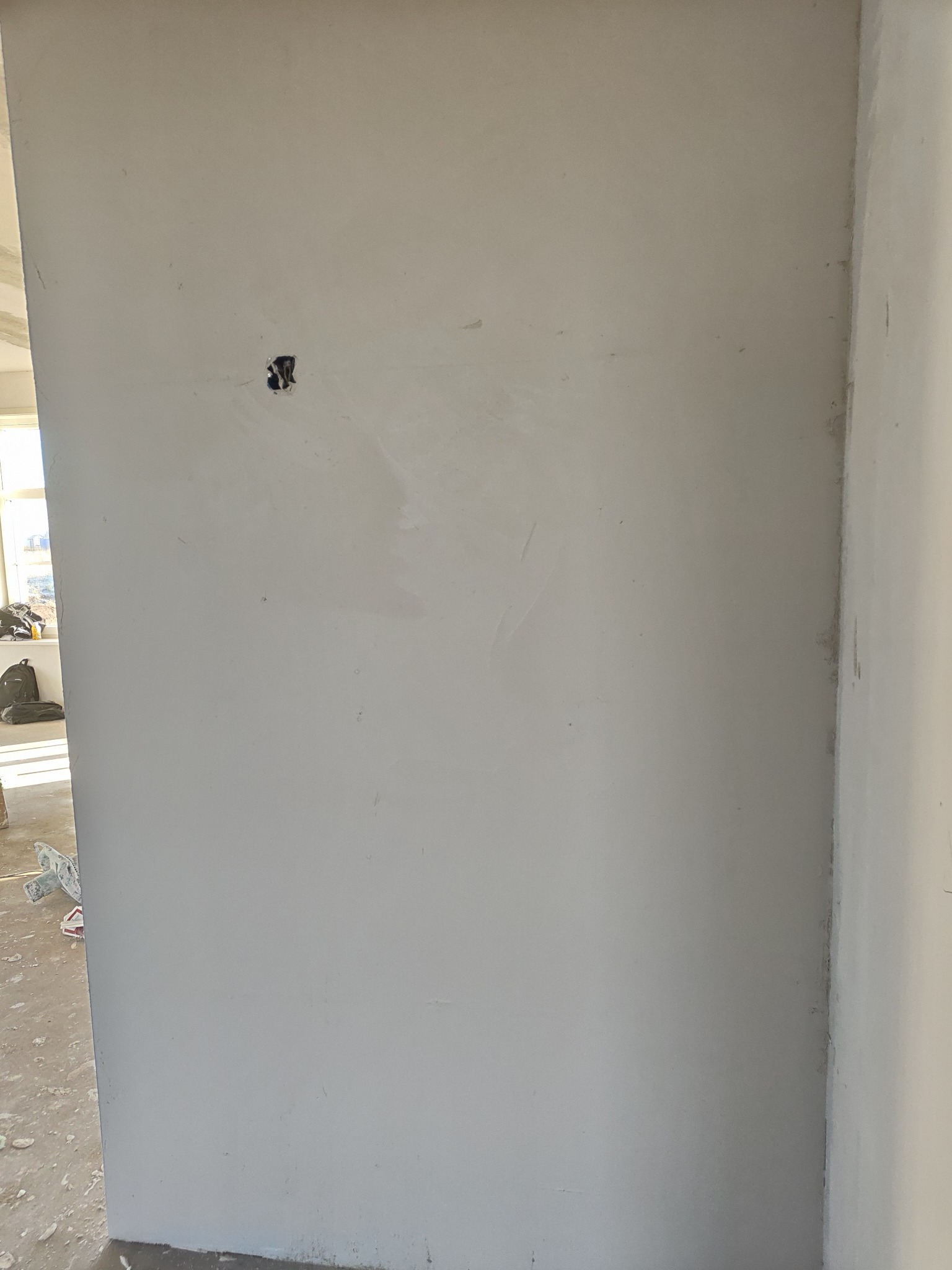 Ściana po szpachlowaniu, przygotowana do malowania, widoczne gniazdko elektryczne i niedoskonałości powierzchni