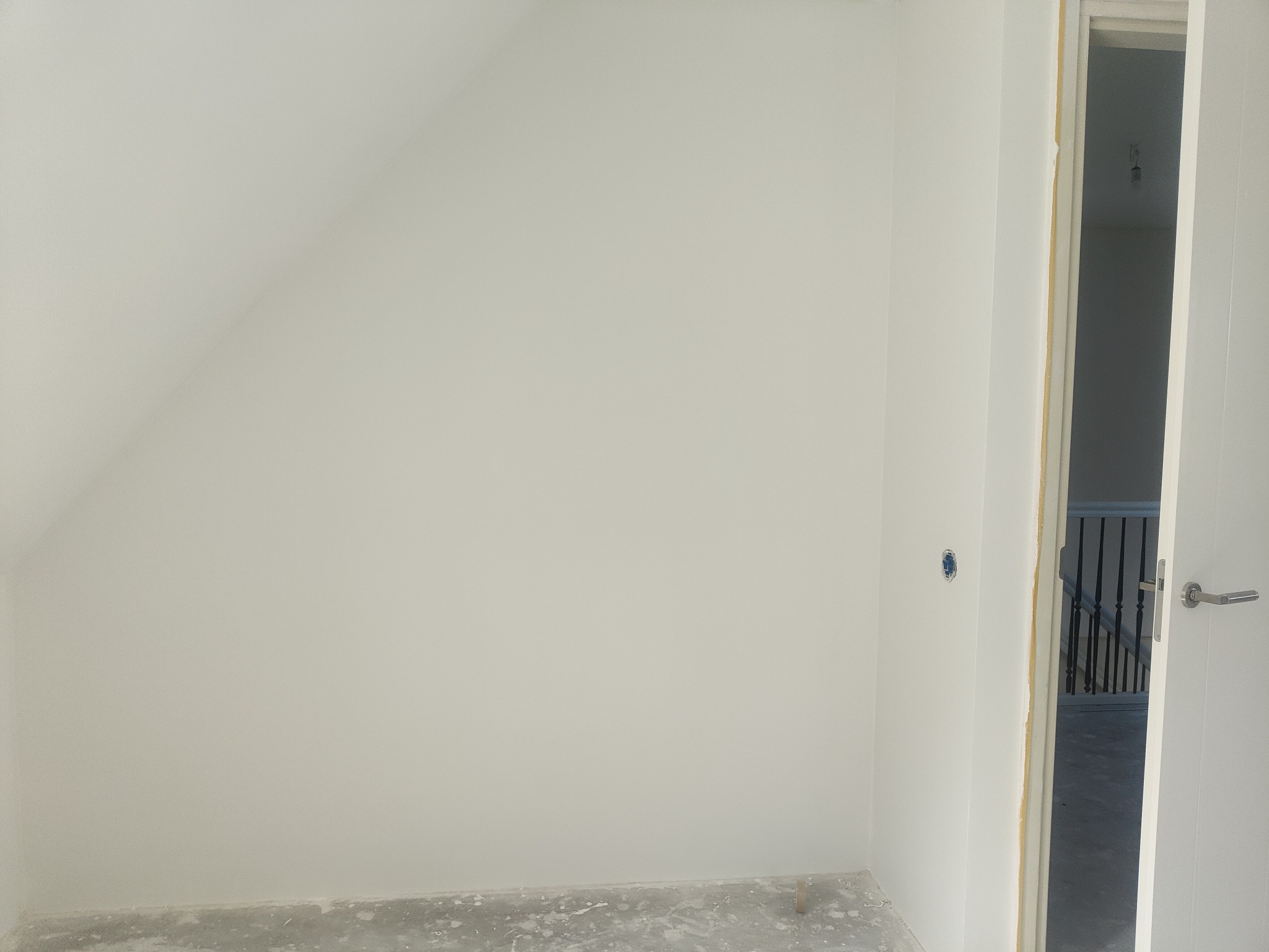 Świeżo pomalowane na biało poddasze ze skosami, widoczny fragment gniazdka elektrycznego i otwarte drzwi z widokiem na schody.