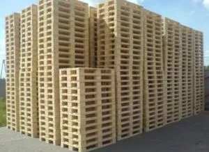 Stosy jasnych, drewnianych palet ustawione na zewnątrz, widoczne z perspektywy lekko od dołu.