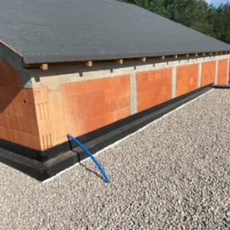 Nowoczesny dach płaski pokryty papą, zabezpieczony obróbką blacharską i warstwą żwiru, z widoczną niebieską rurą odprowadzającą wodę.