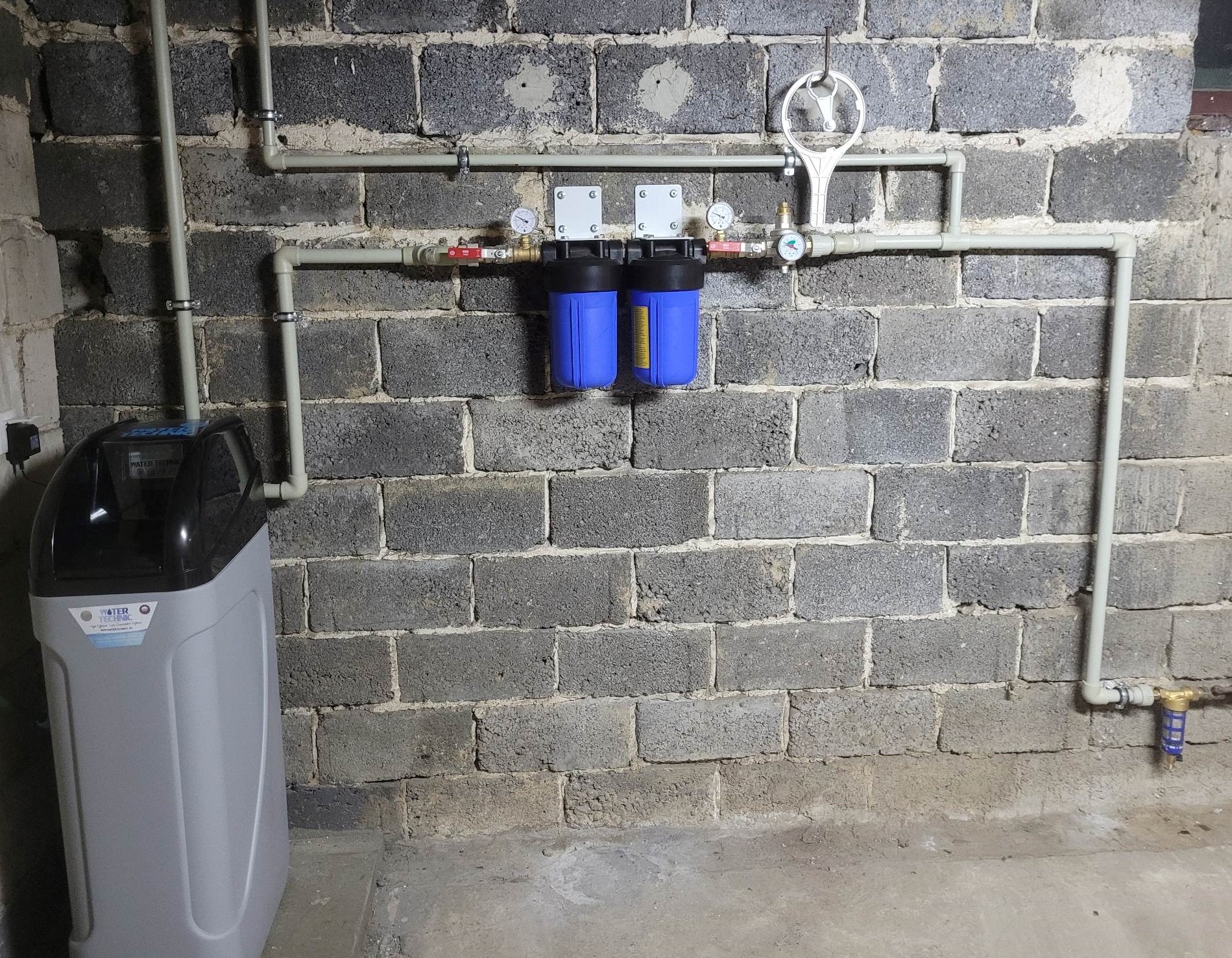 Zestaw filtrów wody Big Blue z reduktorem Afriso i zmiękczacz wody Water Technic zamontowane na tle ściany z szarego betonu komórkowego.