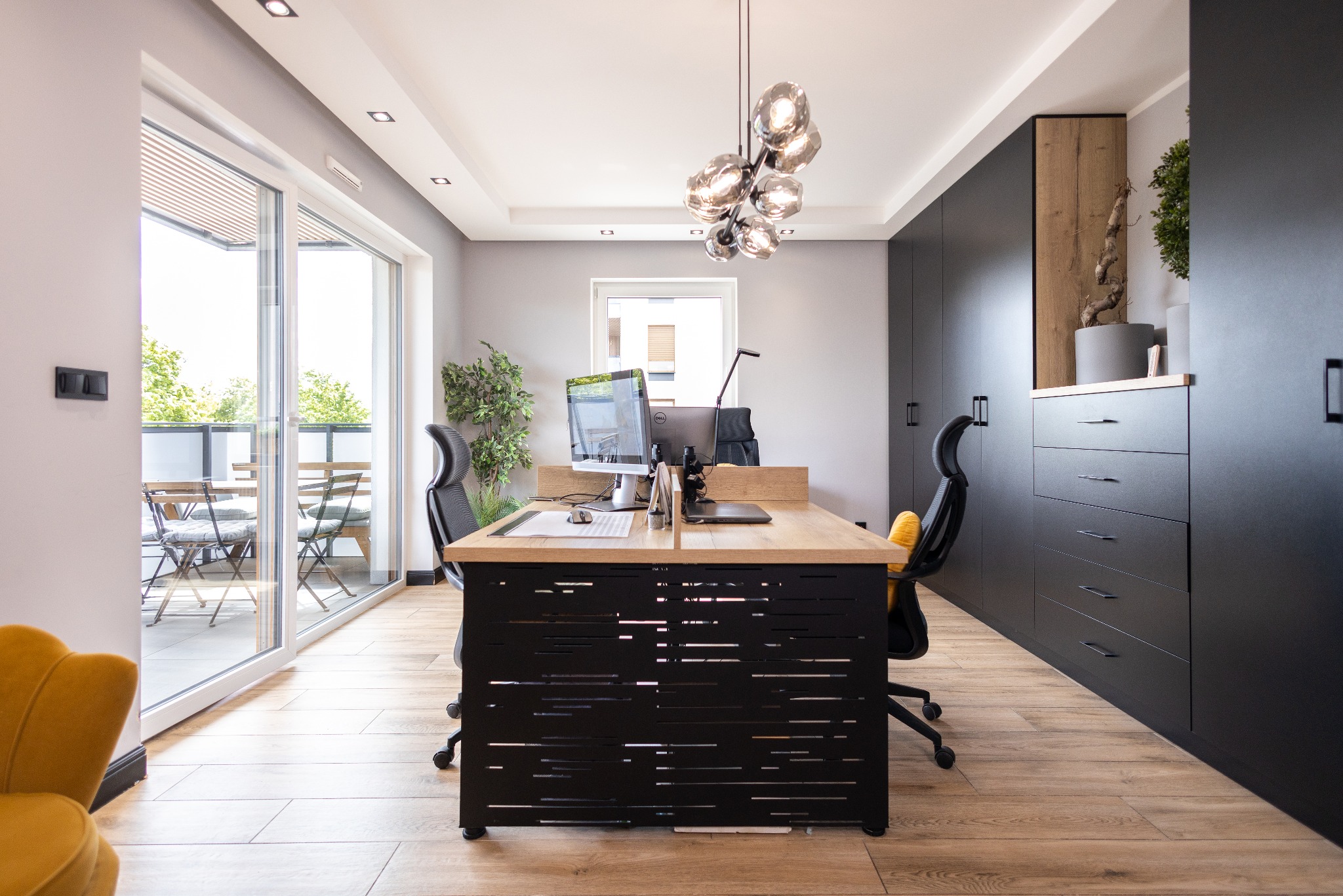 Nowoczesne wykończenie wnętrza biura w Bydgoszczy: jasne podłogi, designerski stół z czarnymi detalami, szafy w zabudowie i balkon z widokiem na zieleń.
