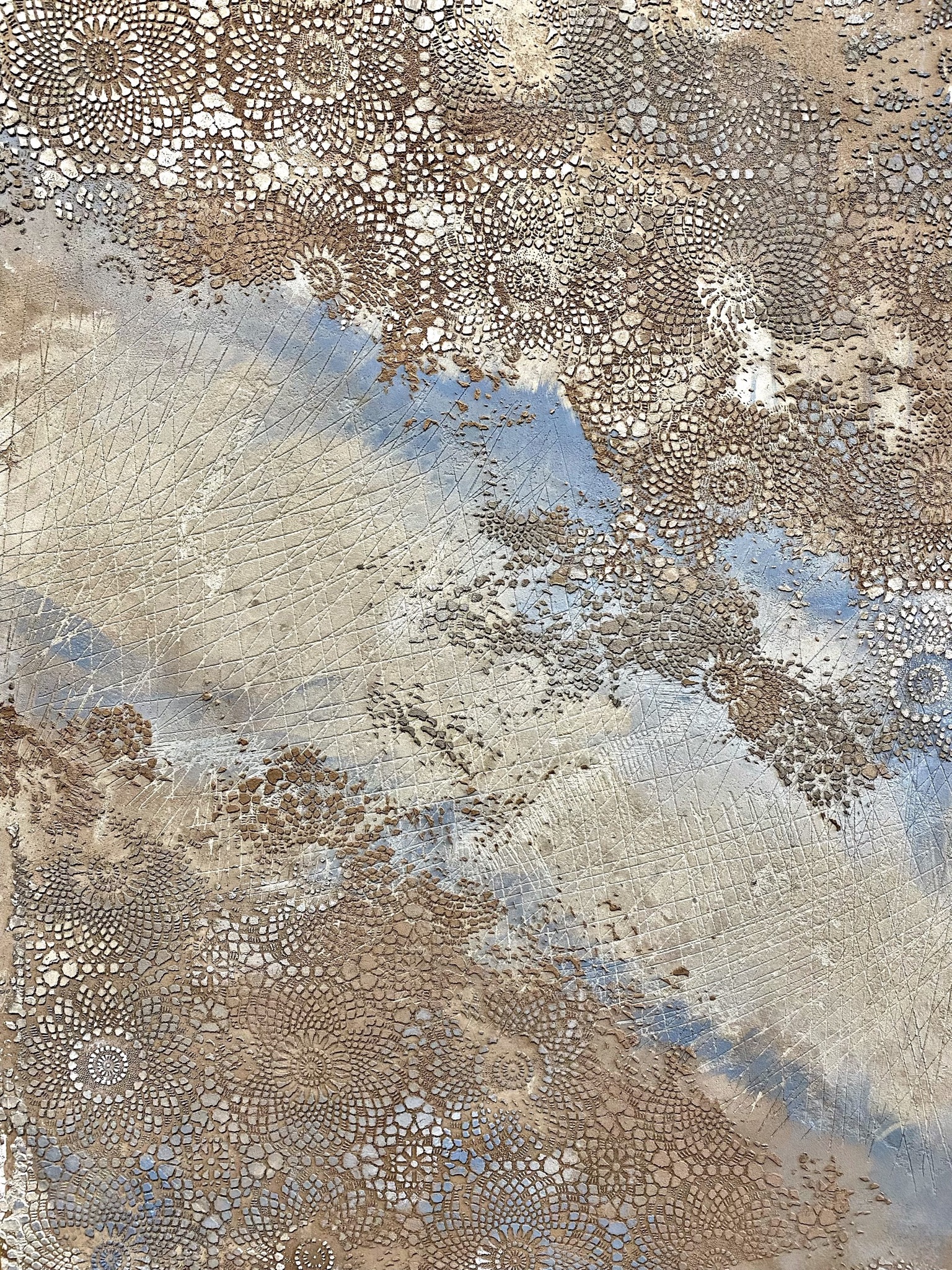 Szczegółowe ujęcie powierzchni z efektem strukturalnym przypominającym koronki i siatkę, w odcieniach beżu, brązu i błękitu, tworzące artystyczny wzór na posadzce.
