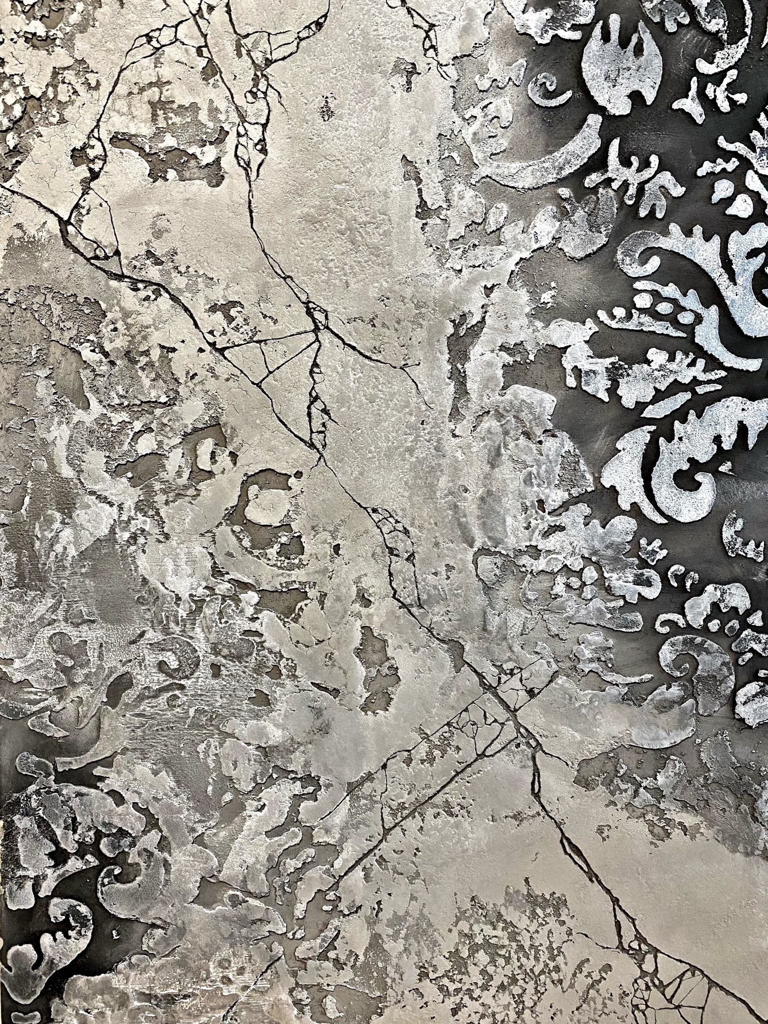 Szara, teksturowana powierzchnia z pęknięciami i dekoracyjnymi, srebrnymi wzorami na ciemnym tle.