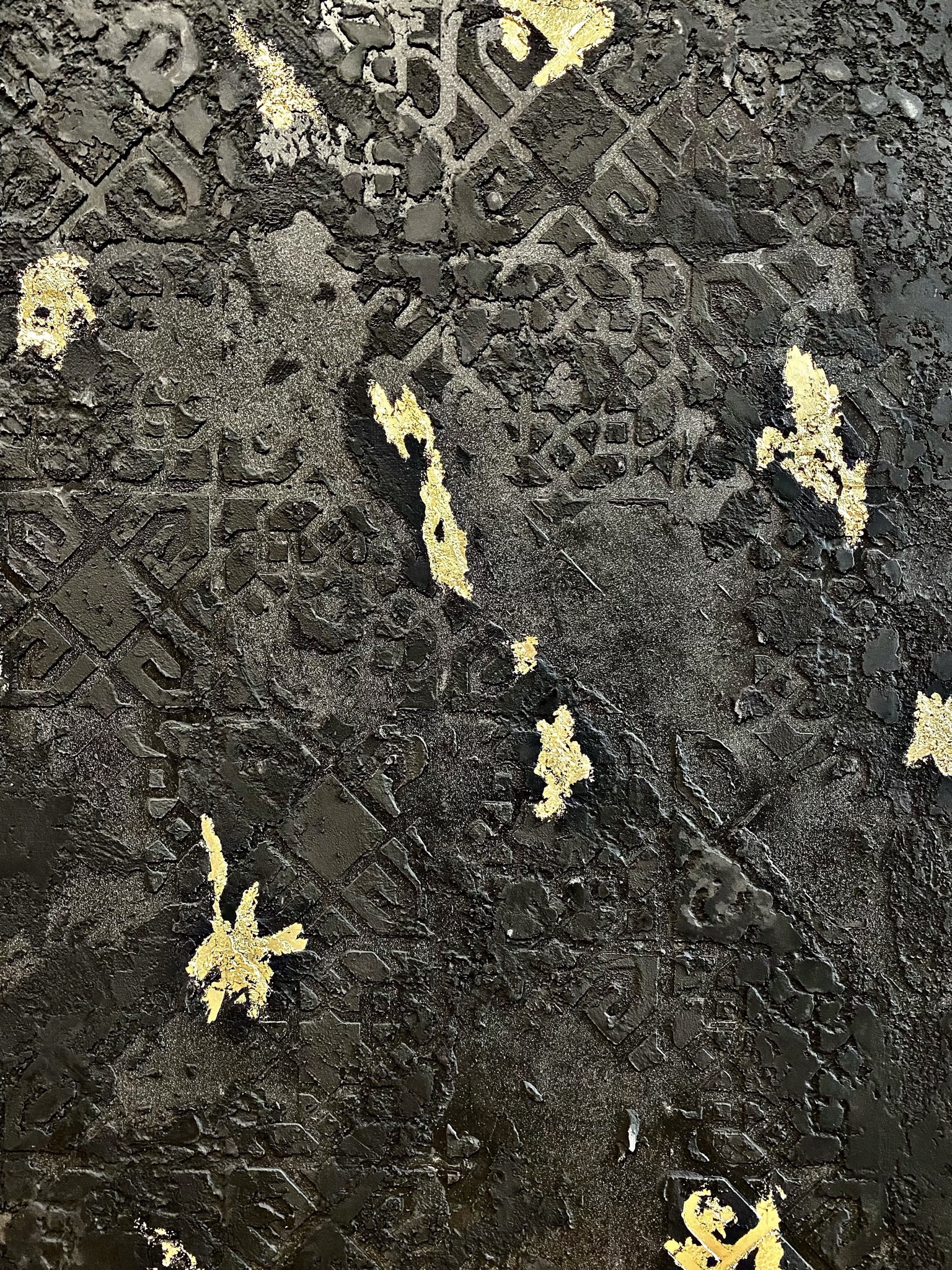 Czarna, teksturowana powierzchnia z wytłoczonym wzorem geometrycznym i nieregularnymi płatkami złota.