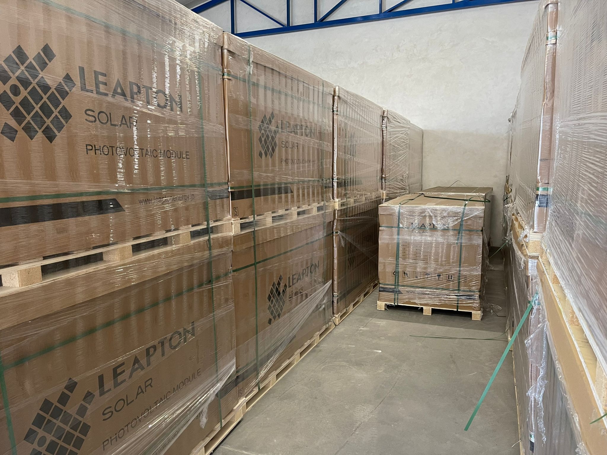 Składowane na paletach, owinięte folią stretch panele słoneczne Leapton Solar w magazynie. Widoczne logo producenta i informacje o produkcie na kartonach.