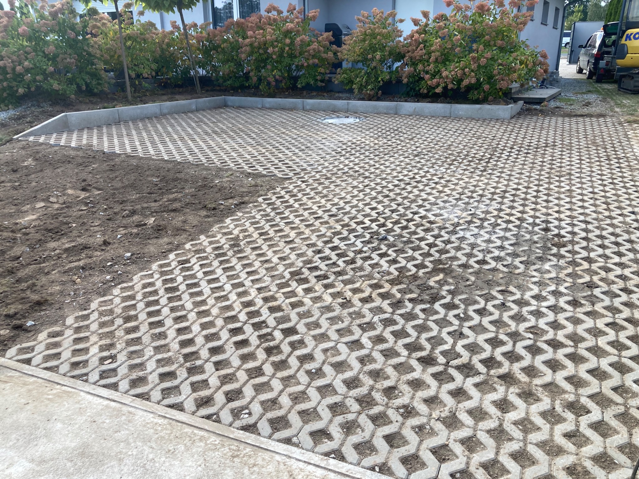 Częściowo ułożona ażurowa nawierzchnia z betonowych płyt na podjeździe, obrzeża betonowe, widoczne fragmenty ziemi przed ukończeniem prac.