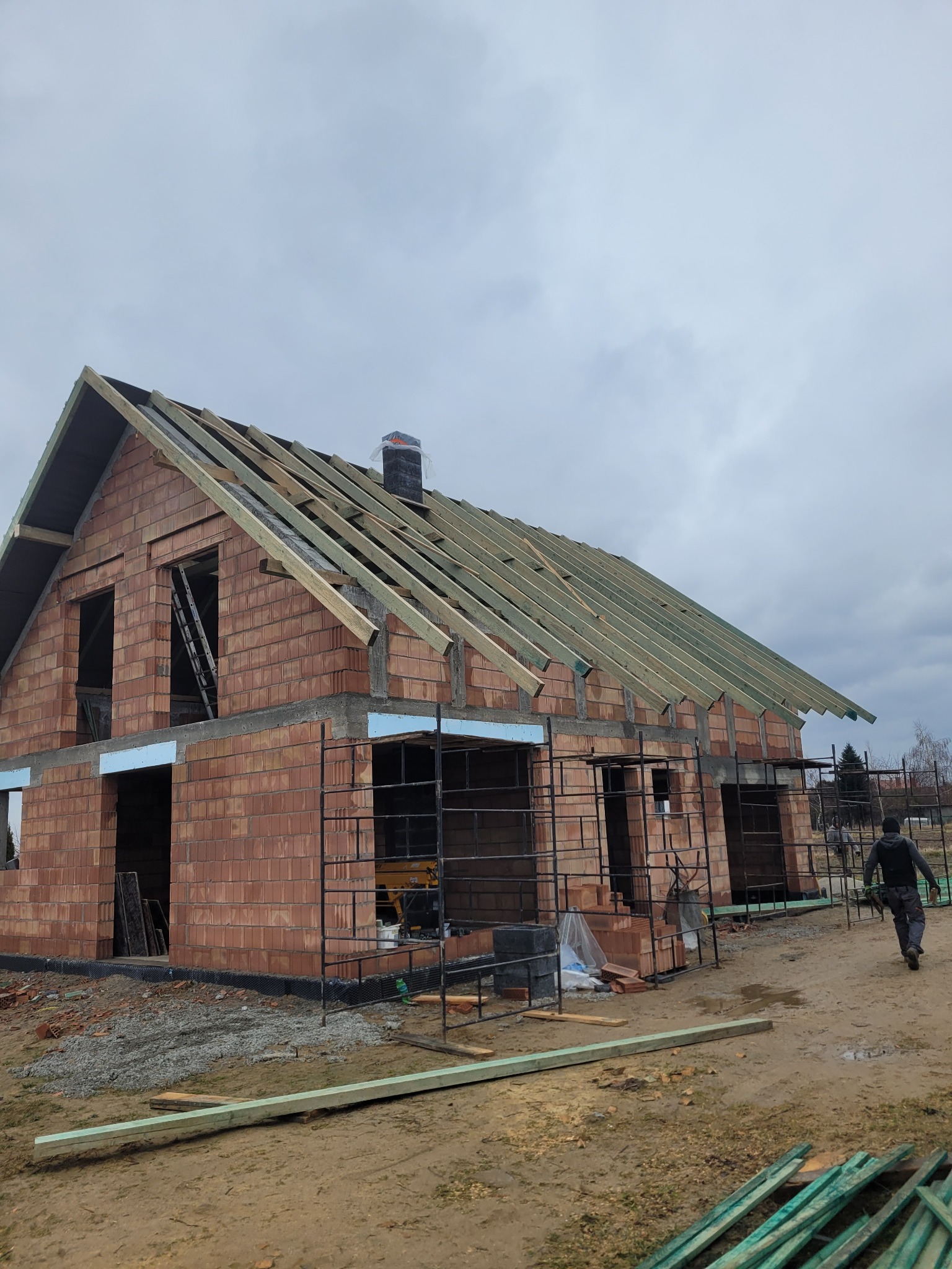 Budowa domu jednorodzinnego w Żabnie w trakcie montażu więźby dachowej, widoczne elementy konstrukcyjne dachu i komin zabezpieczony folią.