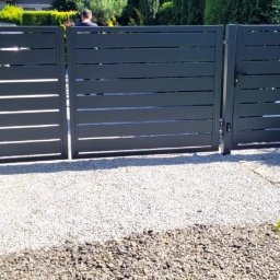 Karol Górny usługi spawalnicze - Bramy - Balustrady - Antracytowa brama wjazdowa z poziomymi lamelami i zintegrowaną furtką, zamontowana na żwirowym podjeździe, z widoczną skrzynką pocztową '4A UL LEŚNA' i dekoracjami roślinnymi.