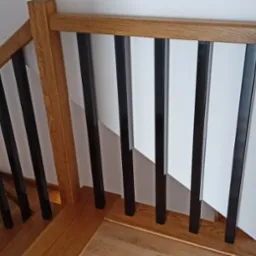 Fragment drewnianych schodów z balustradą z czarnymi, metalowymi prętami, oświetlenie LED na ścianie