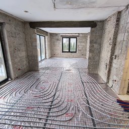 INSTALACJE CHROSTOWSKI Marcin Chrostowski - Rozłożona instalacja ogrzewania podłogowego w surowym wnętrzu z widocznymi przewodami grzewczymi na folii z siatką, przygotowana do zalania wylewką.