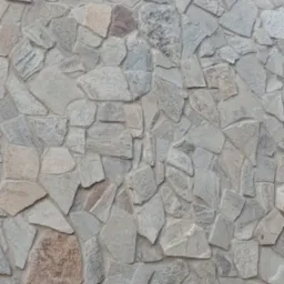 Ściana zewnętrzna wykończona nieregularnymi, szarymi kamieniami o zróżnicowanej fakturze, z fragmentem drewnianego elementu w lewym dolnym rogu.