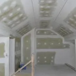 Poddasze w trakcie zabudowy płytami gipsowo-kartonowymi, widoczne stelaże i wstępnie zamontowane płyty z widocznymi śladami szpachlowania, nieregularny kształt pomieszczenia.