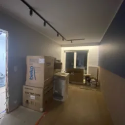 Wnętrze w trakcie remontu: widoczne kartony z nowym sprzętem AGD (piekarnik Samsung, pralka Beko), panele podłogowe, ściana pomalowana na dwa kolory, listwy przypodłogowe, oświetlenie szynowe...