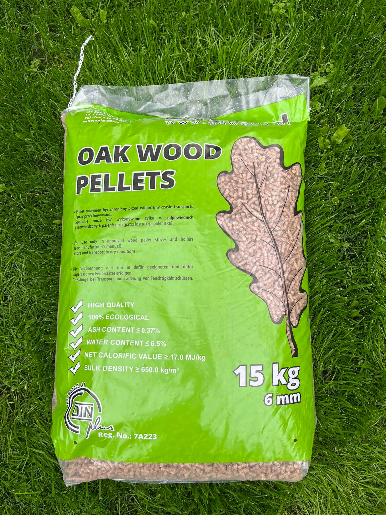 Worek zielonego pelletu drzewnego Oak Wood o wadze 15 kg, leżący na trawie, z widocznymi specyfikacjami jakości i certyfikatem DIN plus.