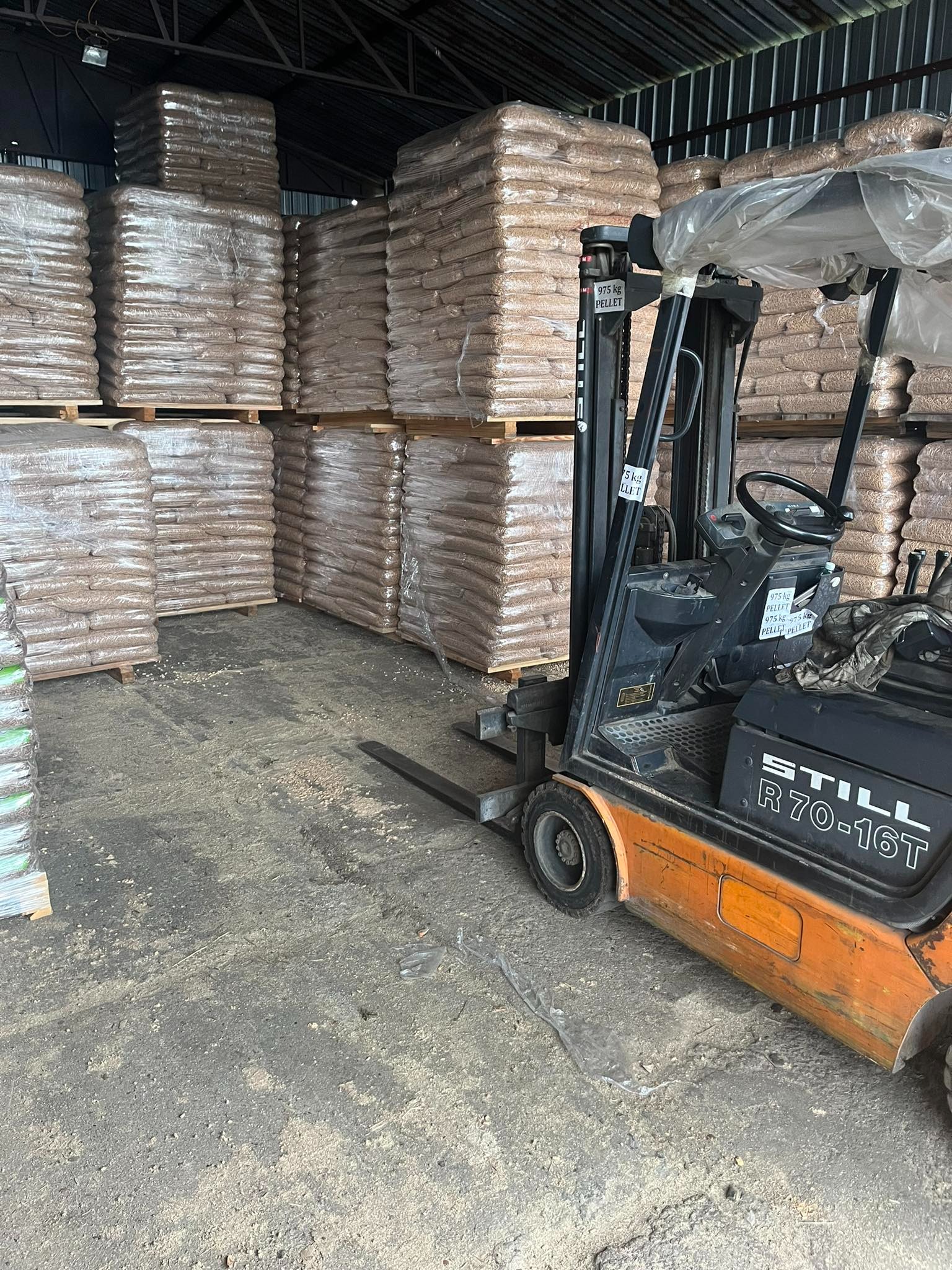 Magazyn z ułożonymi na paletach workami pelletu, widoczny wózek widłowy Still R70-16T z informacją o wadze pelletu 975kg na boku.