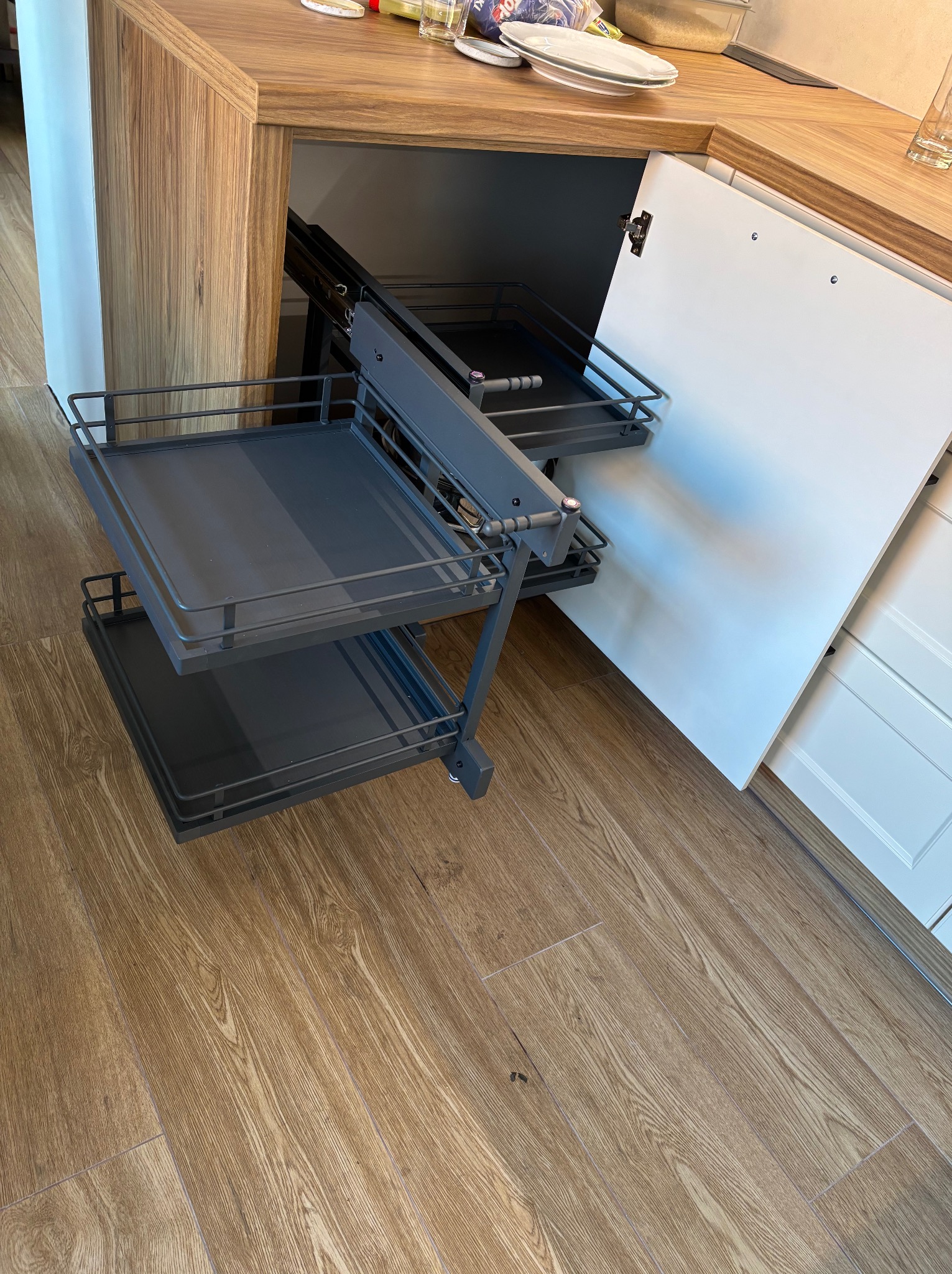 Wysuwany, dwupoziomowy kosz cargo w narożnej szafce kuchennej z drewnianym blatem i białymi frontami. Widoczna struktura drewna na blacie.