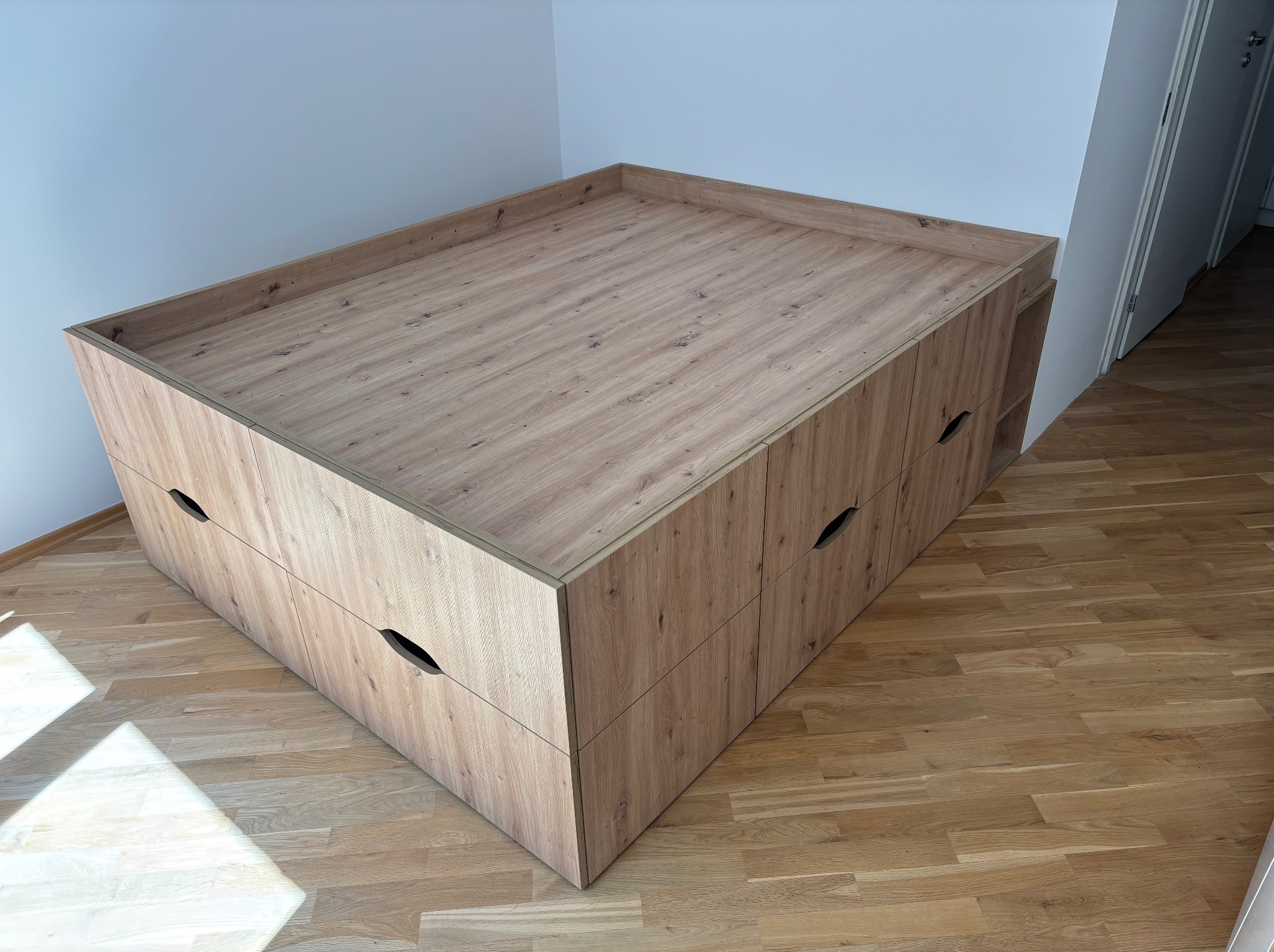Drewniana szafka z szufladami i otwartą półką, wykonana na wymiar, w jasnym wnętrzu. Widoczna struktura drewna i minimalistyczne uchwyty.