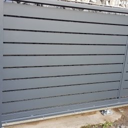 E&P PRO-METAL spółka jawna E.Luty P.Luty - Szara, przesuwna brama wjazdowa z poziomymi panelami, widoczne elementy automatyki i napędu, tło z kamiennego muru.