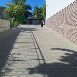 FPMULTISERWIS Fortunata Piec - Ułożona kostka brukowa na podjeździe z widocznymi cieniami drzew, obok ściana z cegły klinkierowej i zaparkowany śmieciowóz w tle.