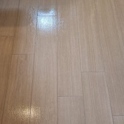 FPMULTISERWIS Fortunata Piec - Świeżo umyte, błyszczące płytki podłogowe imitujące drewno, z widocznymi smugami wody i fragmentem białej wanny w rogu.
