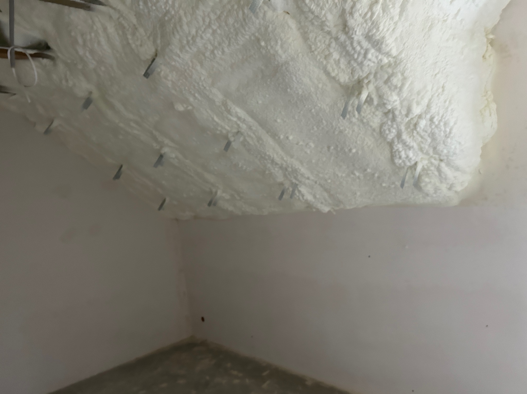 Poddasze po ociepleniu pianką PUR, widoczne metalowe elementy mocujące. Ściany pomalowane na jasny kolor. Fragment betonowej podłogi.