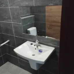 Nowoczesna łazienka z umywalką na postumencie, szarą płytką imitującą kamień i lustrem, w którym odbija się toaleta