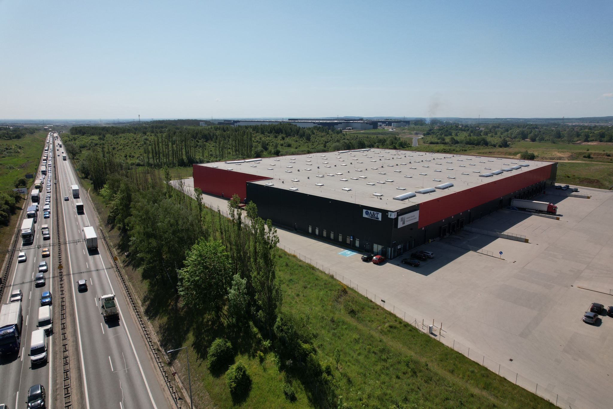 Szeroki plan magazynu z rampami załadunkowymi, widok z góry, obok ruchliwa autostrada i tereny zielone.