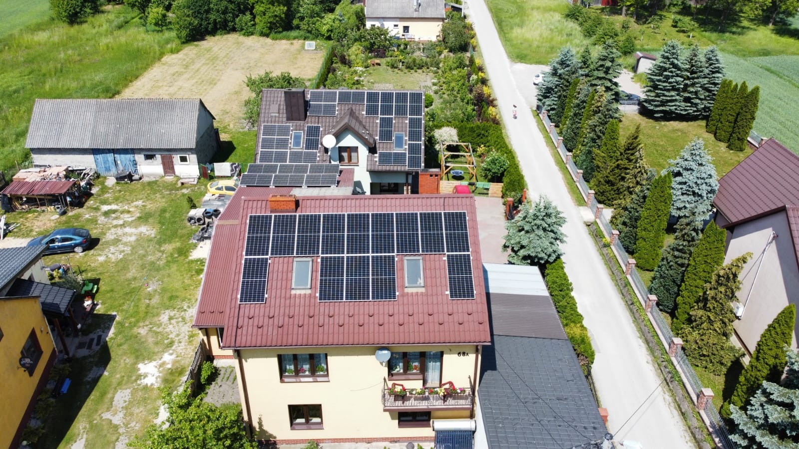 Widok z lotu ptaka na dwa domy jednorodzinne z panelami słonecznymi na dachach w słoneczny dzień. Na dachu jednego z domów widoczne okna dachowe pomiędzy panelami.
