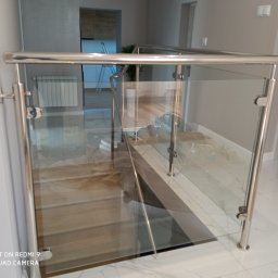 Balustrady Maciejewski - Szklana balustrada ze stalowymi słupkami zamontowana przy schodach wewnętrznych, widoczne mocowania szkła do słupków, marmurowa podłoga.