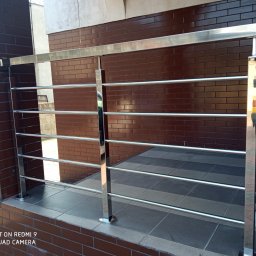 Balustrady Maciejewski - Błyszcząca, chromowana barierka z poziomymi prętami, zamontowana na ceglanym murku, z widocznym fragmentem wyłożonej płytkami podłogi.