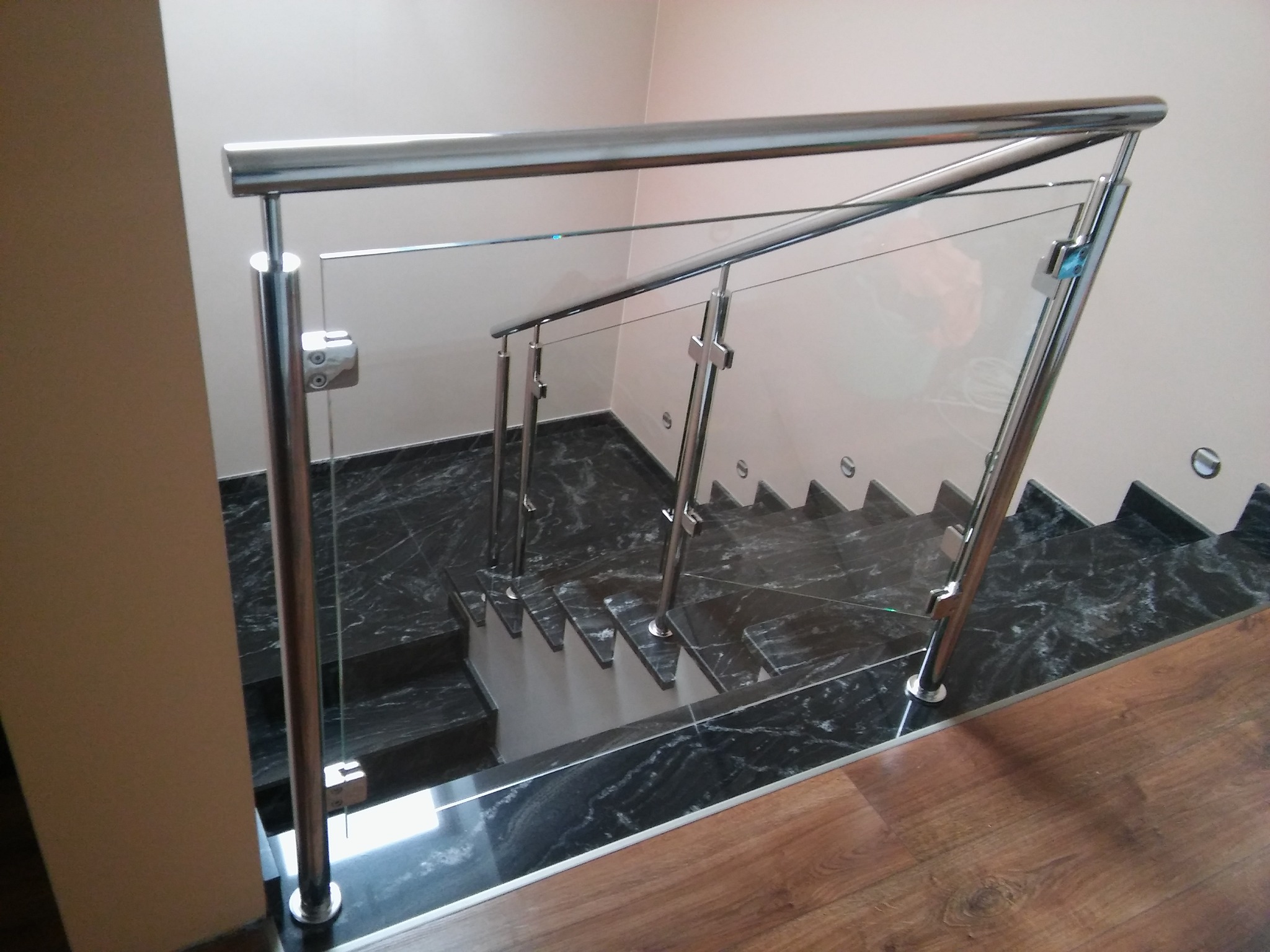 Szklana balustrada ze stalowymi słupkami na schodach z ciemnego marmuru, widok z góry.