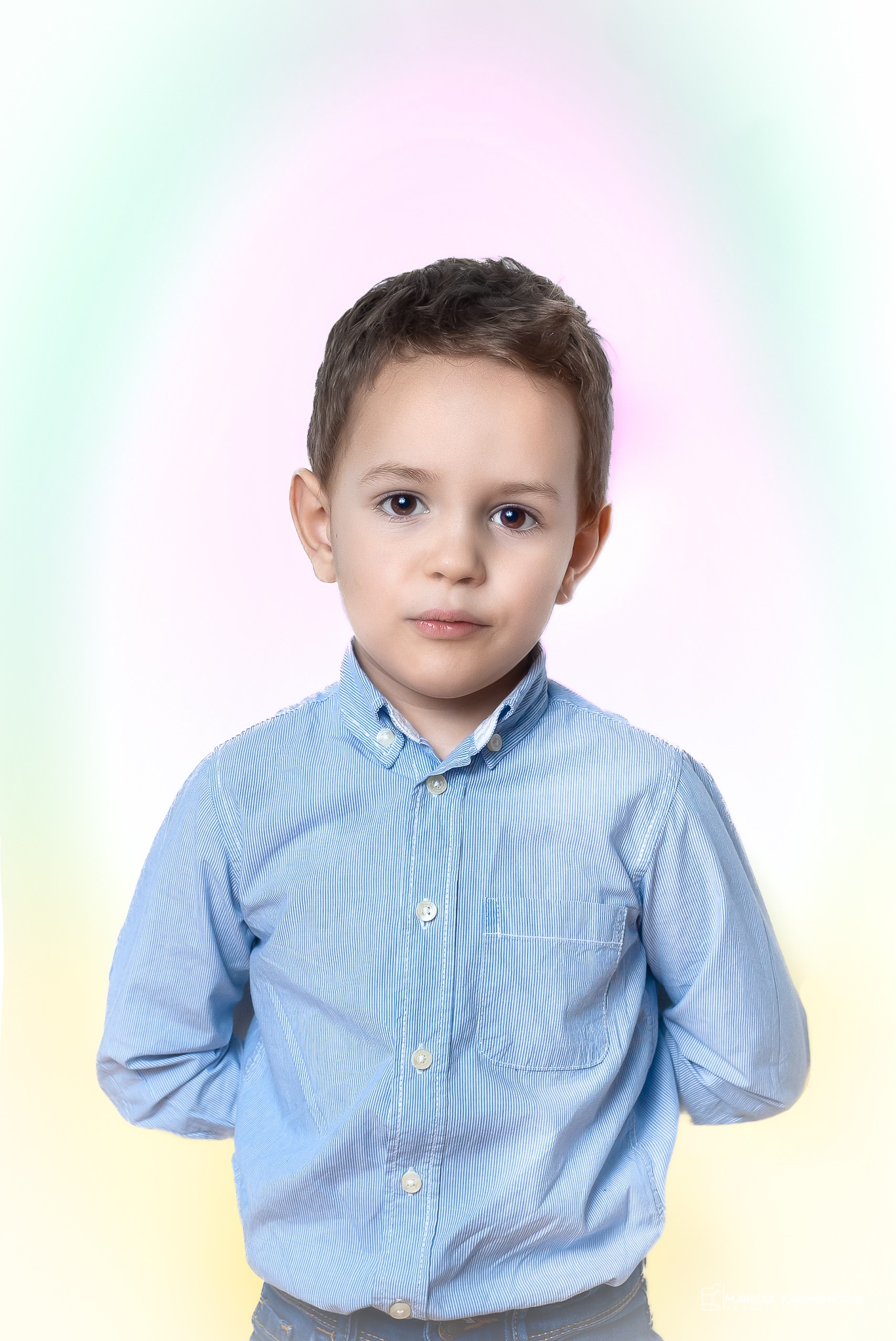 Portret młodego chłopca w niebieskiej koszuli z długim rękawem na rozmytym, pastelowym tle.