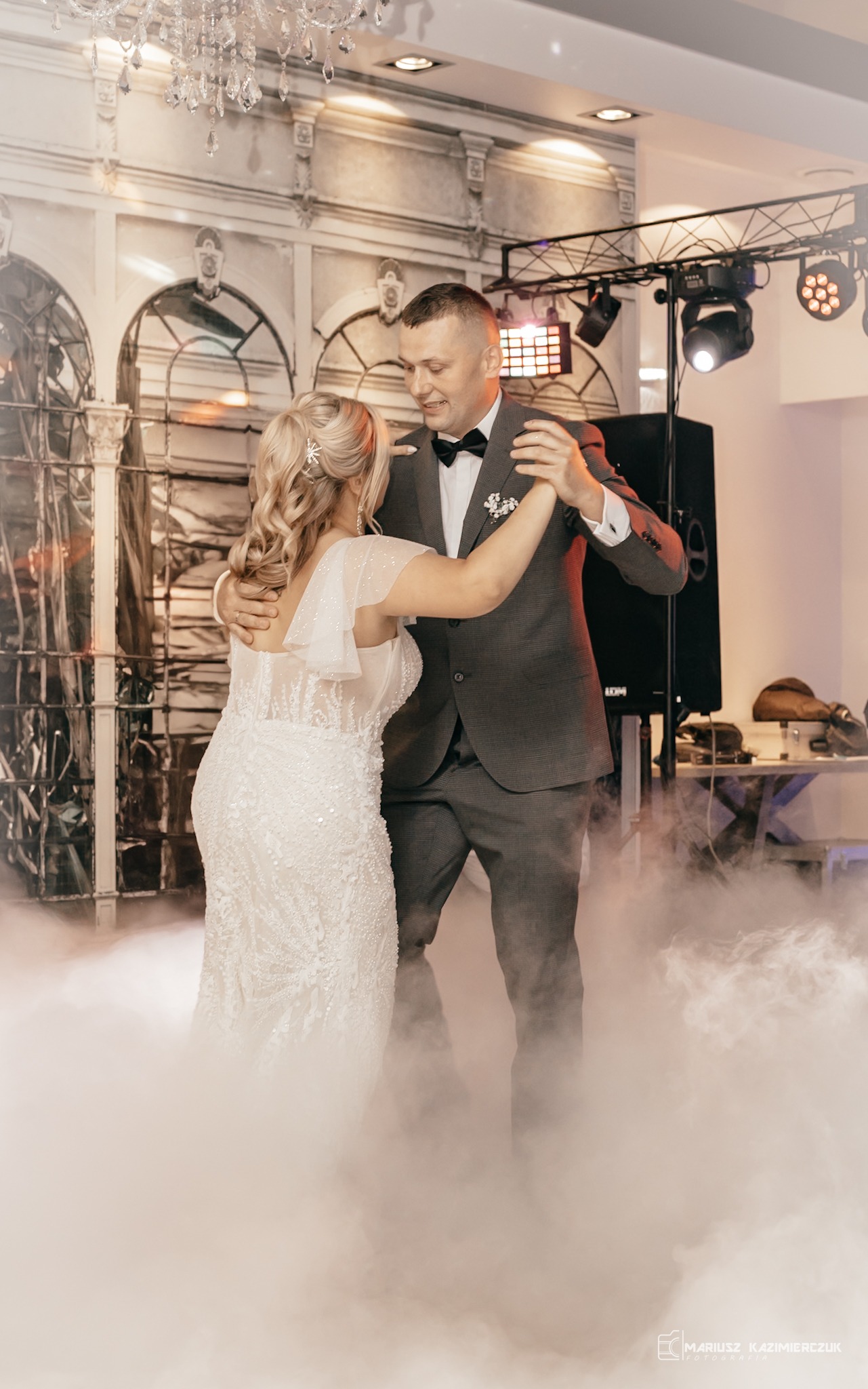 Para młoda tańczy pierwszy taniec w dymie, oświetlenie sceniczne, dekoracje weselne w tle.