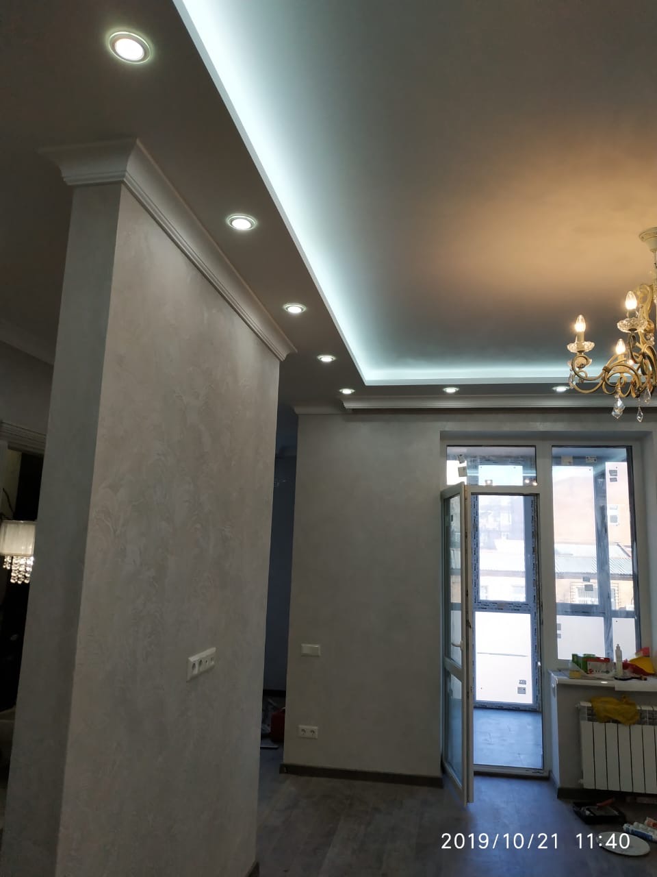 Wykończone wnętrze pokoju z kolumną dekoracyjną, oświetleniem punktowym w suficie podwieszanym i żyrandolem w stylu retro.