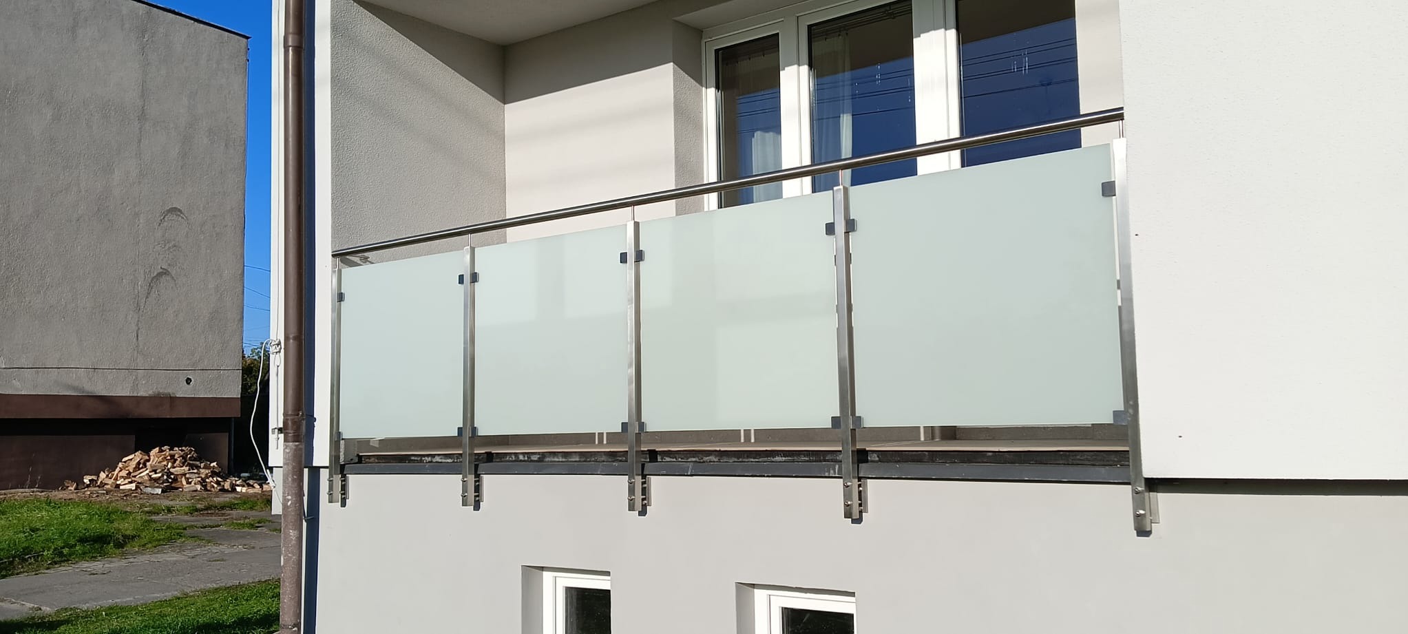 Balkon z nowoczesną balustradą ze stali nierdzewnej i mlecznego szkła, widok z dołu, jasne światło.