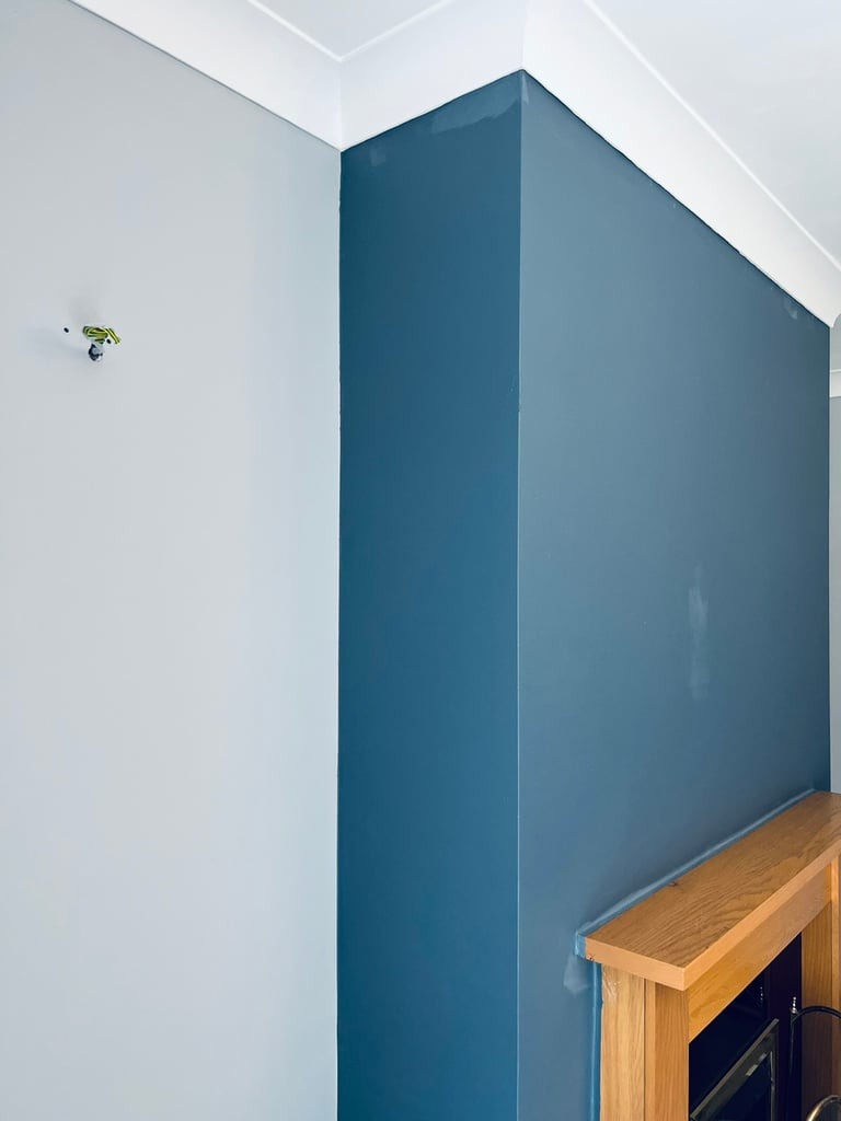 Ściana pomalowana na dwa kolory: szary i granatowy, z drewnianą obudową kominka w dolnej części, widoczne ślady po taśmie malarskiej