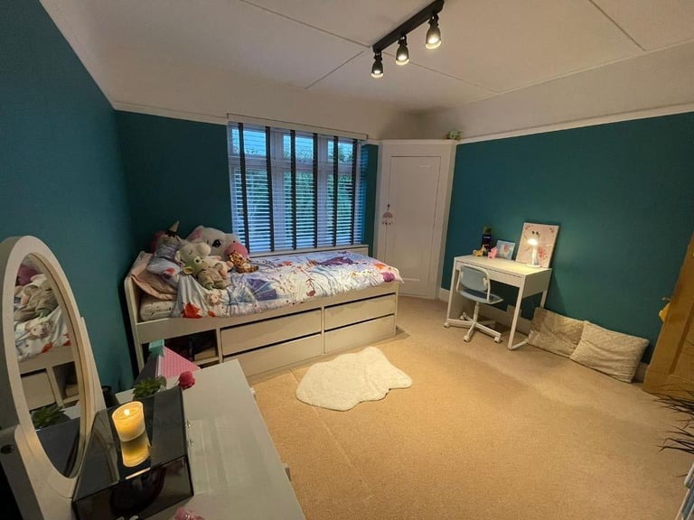 Pokój dziecięcy z turkusowymi ścianami, białymi meblami i beżową wykładziną, oświetlony trzypunktową lampą sufitową.