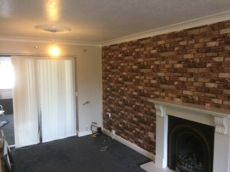 Salon z tapetą imitującą cegłę na ścianie, biały kominek i zasłonięte pionowe żaluzje okienne.