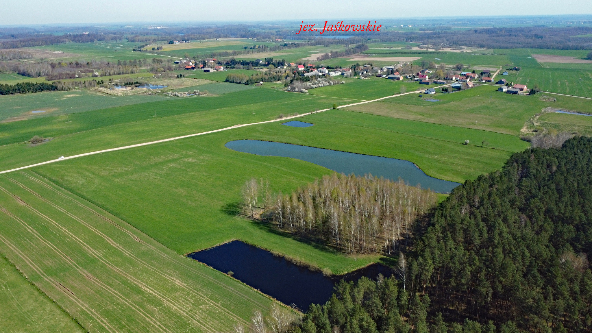 Panoramiczny widok z lotu ptaka na wiejski krajobraz z polami, lasami i jeziorami, w oddali zabudowania wsi Jaśkowskie.