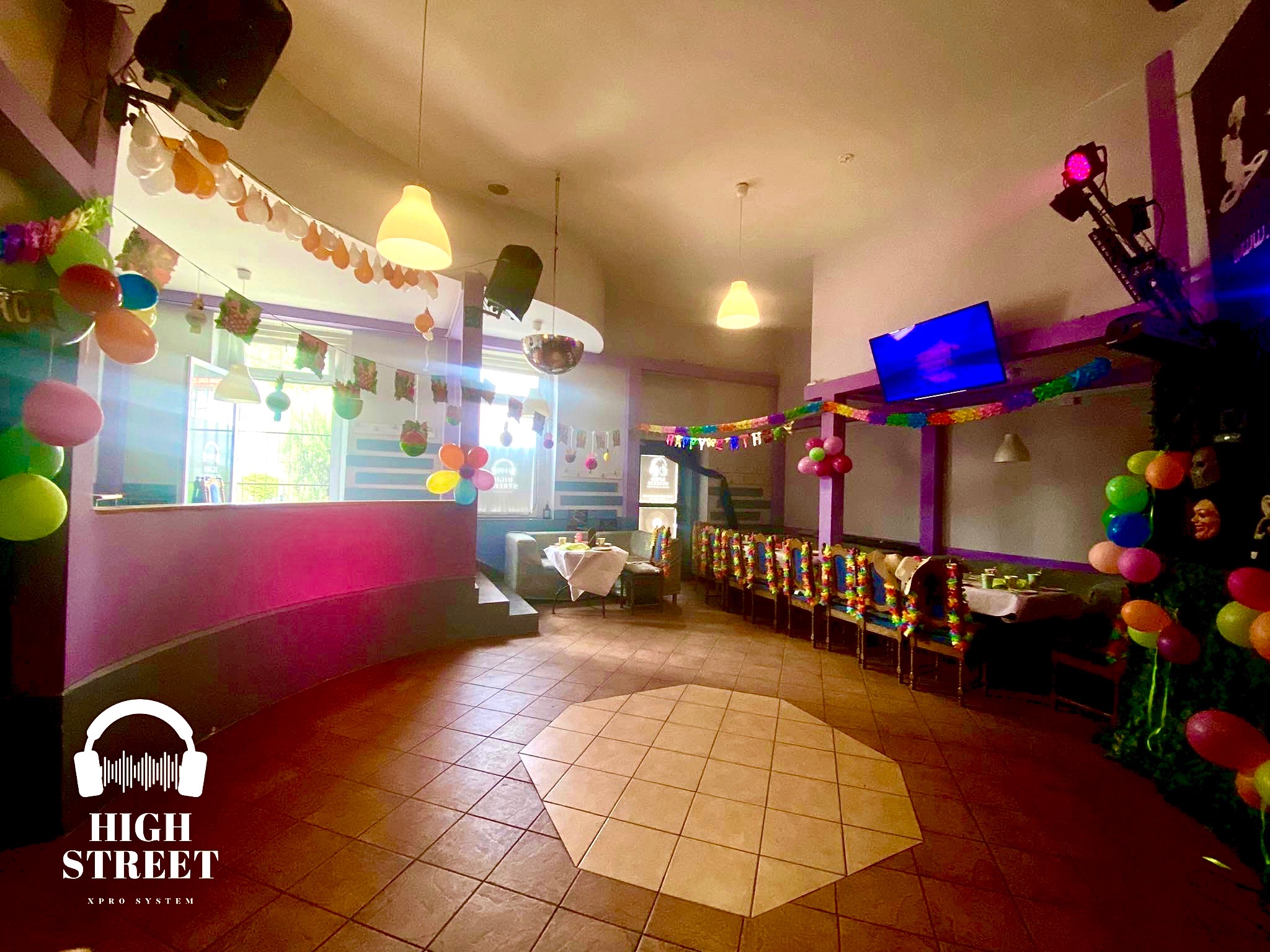 Sala udekorowana na przyjęcie z balonami, girlandami i oświetleniem, widoczny parkiet taneczny i ustawione stoły z krzesłami.