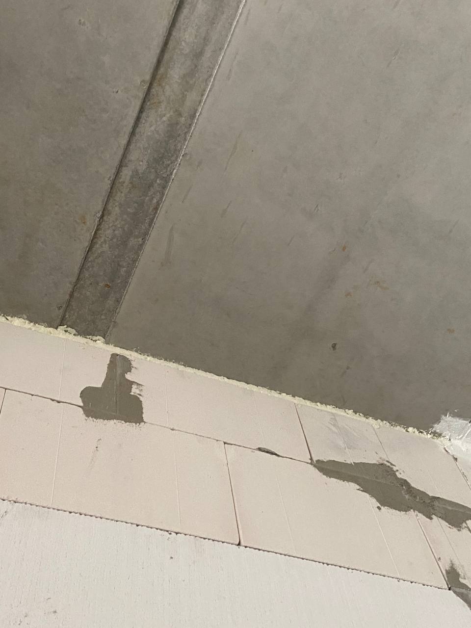 Wnętrze w trakcie budowy: Ściana z białych bloczków z widocznymi śladami zaprawy, surowy betonowy sufit z widoczną szyną montażową.