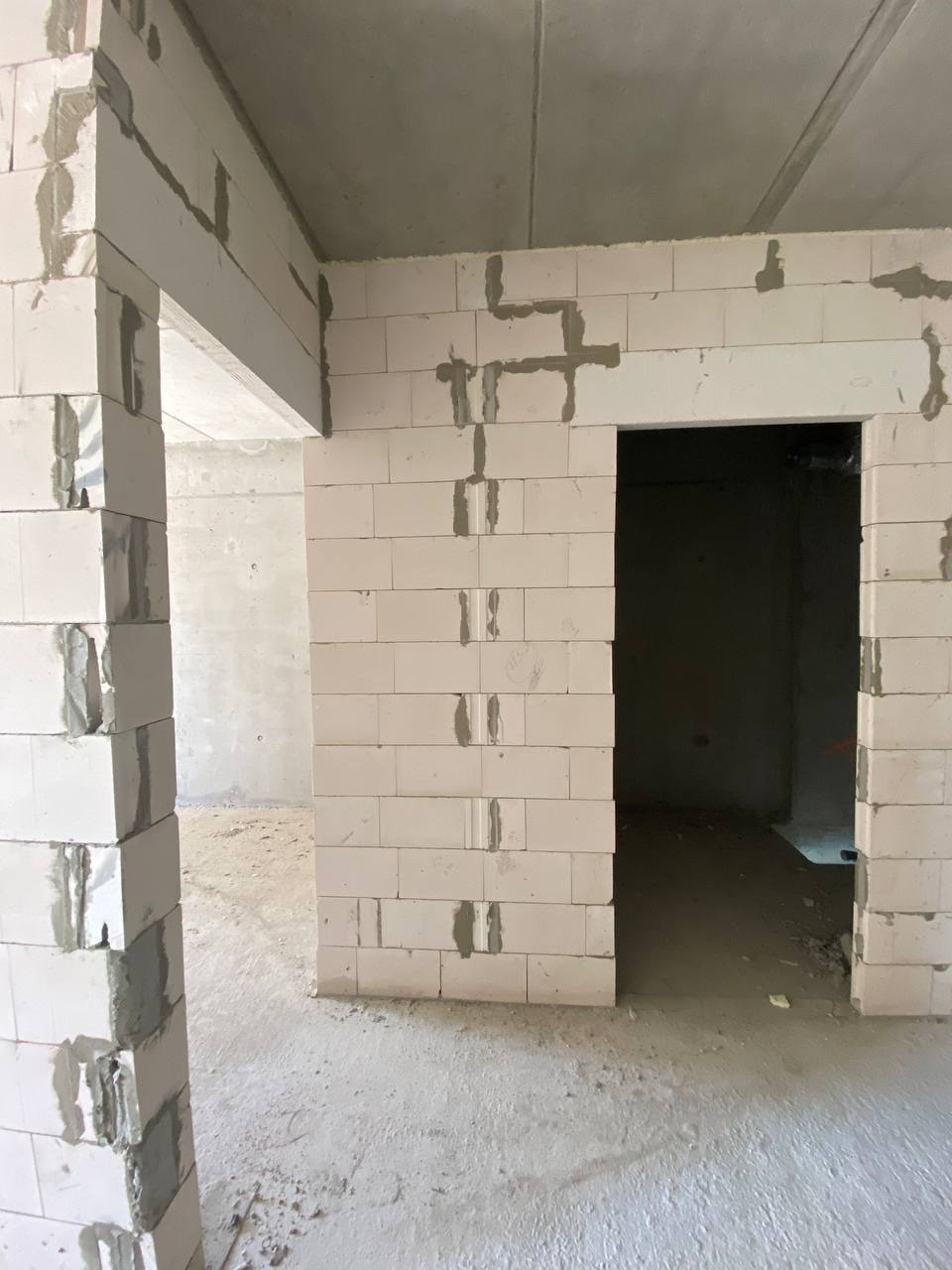 Wnętrze w trakcie budowy z białymi bloczkami, widoczne fragmenty ścian i otwory drzwiowe, ślady zaprawy murarskiej na łączeniach bloczków.