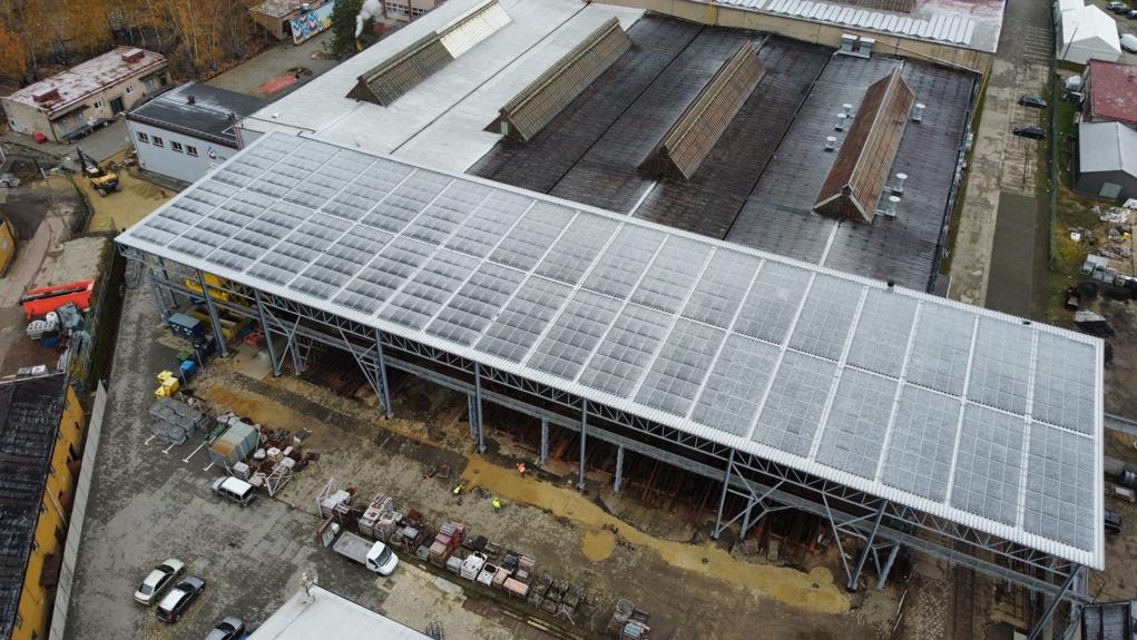 Widok z góry na budowę zadaszenia placu magazynowego z panelami fotowoltaicznymi, widoczne stalowe konstrukcje wsporcze i częściowo ułożone panele słoneczne.