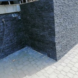 Dawid Szulik - Kąt zewnętrzny wykończony czarnym kamieniem łupkowym, z widocznym kranem i kostką brukową w dwóch odcieniach szarości.